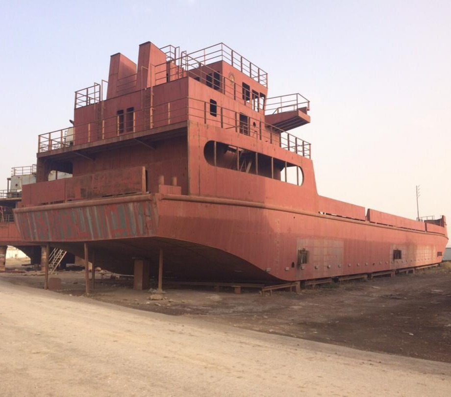 Red-primed steel vessel hull under construction on blocks at the yard