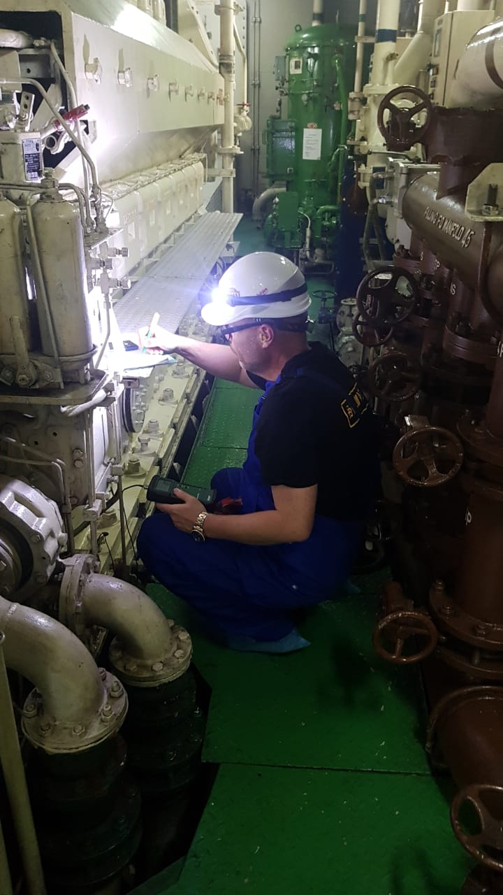 Marine engineer inspecting engine room machinery with a flashlight